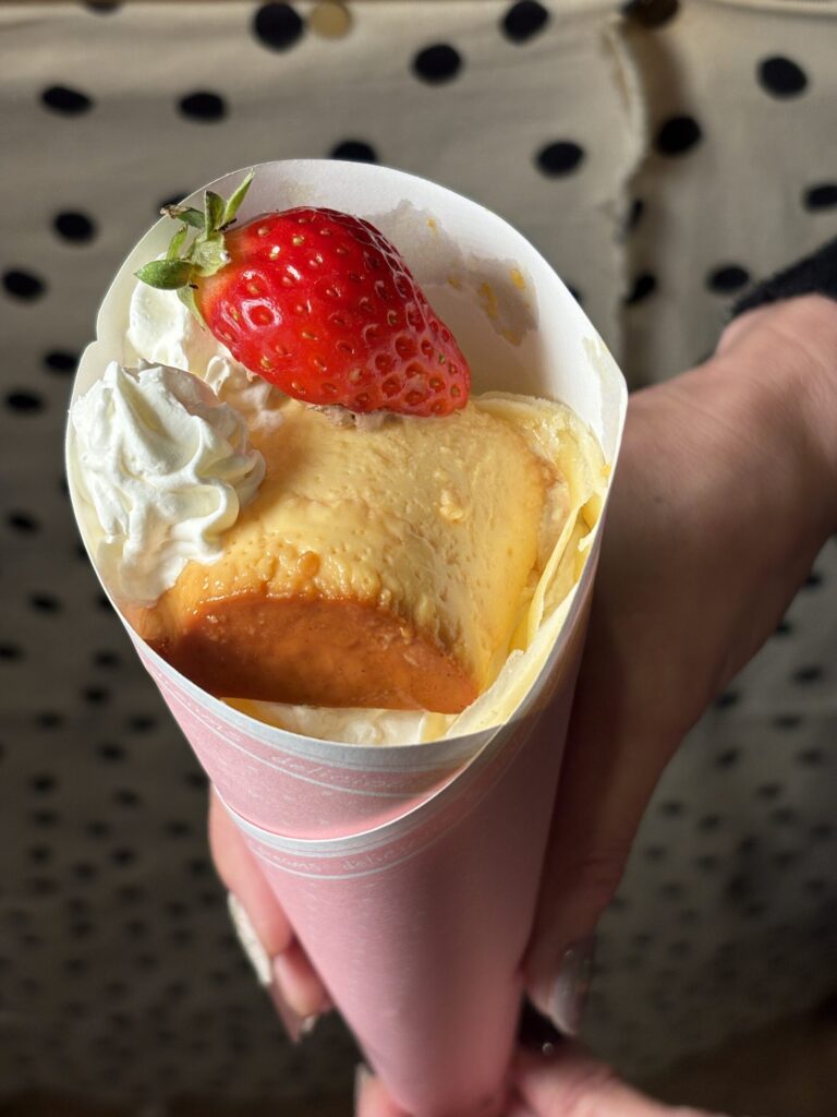 フルーツクレープカップのクローズアップ。ピンクのカップにいちご、イタリアンプリン、ホイップクリーム、両手で優しく持っている様子