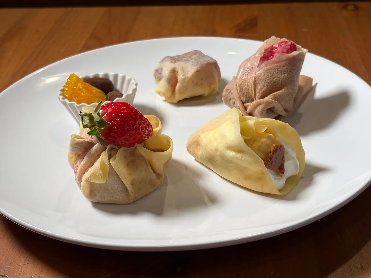 デザートクレープの盛り合わせ。5種類の小さなクレープ、いちご、ベリー、生クリーム、キャラメルソース添え。白い皿に美しく盛り付けられたアソートプレート