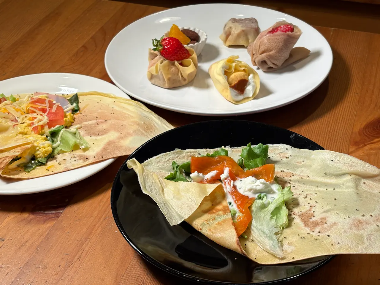 クレープのコースメニュー。スモークサーモンのガクレープ、ハムと卵のクレープ、デザートクレープアソートの3皿セット、木製テーブルに並べられた一式